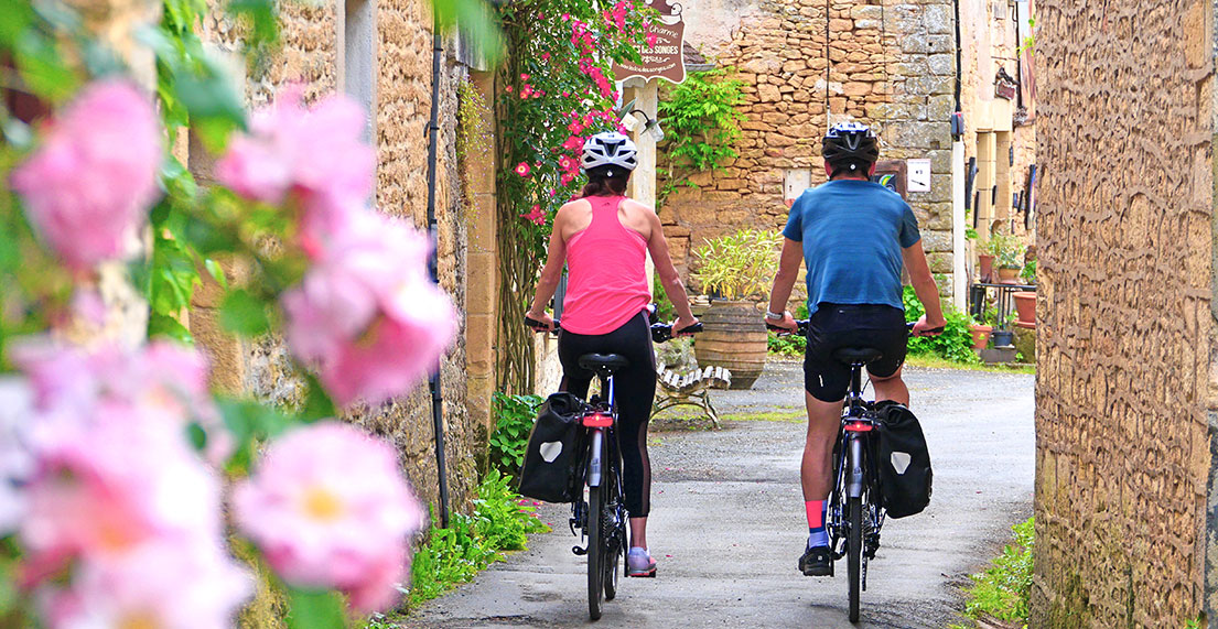 Un couple de cycliste roule sur une petite route de village fleuri