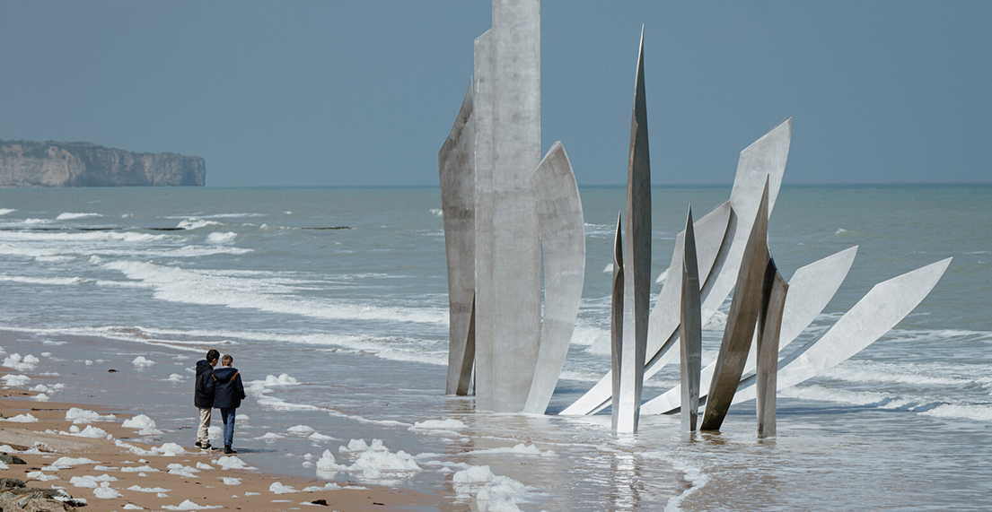 Un couple se promene sur la plage d'Omaha Beach deavant les oeuvres d'arts
