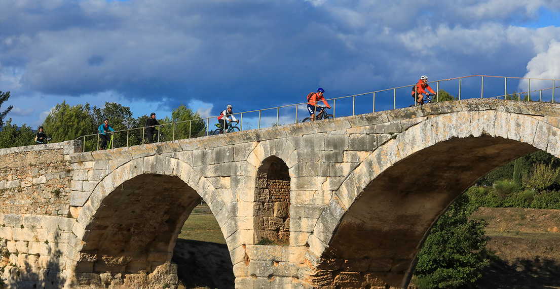 Un groupe de cyclistes traverse un pont en pierres aux arches voutees