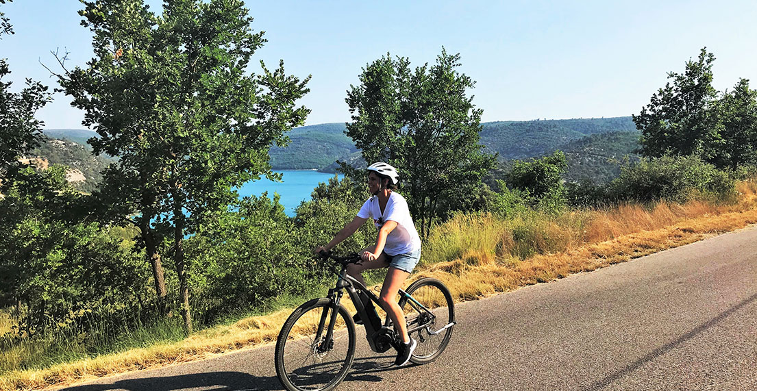 Une cycliste roule devant un lac à l'eau turquoise