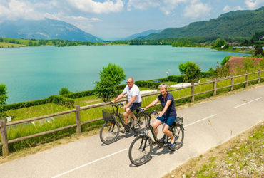 Couple à vélo le long du Rhône sur la ViaRhôna, lac et montagne