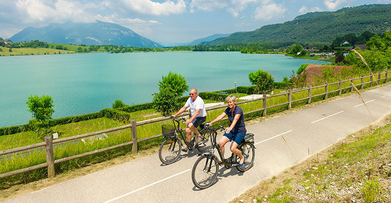 Couple à vélo le long du Rhône sur la ViaRhôna, lac et montagne