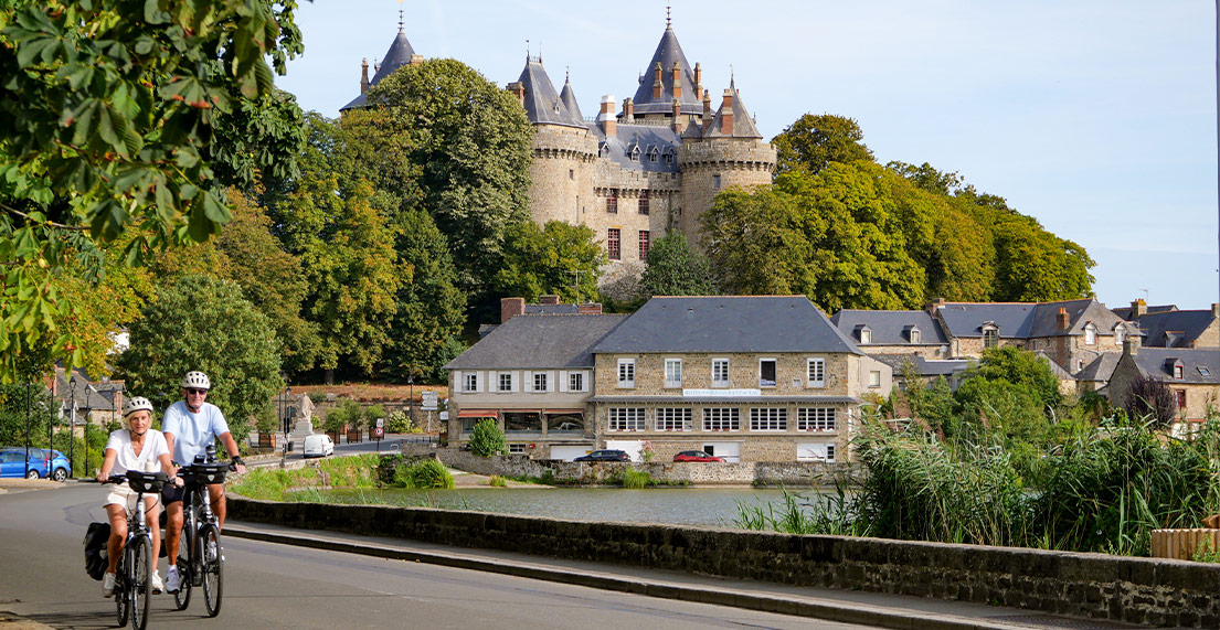 Un couple de cycliste roule sur une route surplombee d un chateau medieval