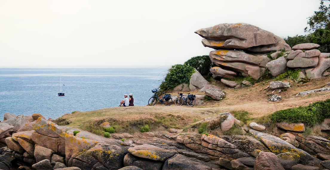 Un couple de cycliste assis face a la mer a cote de rochers de granit rose