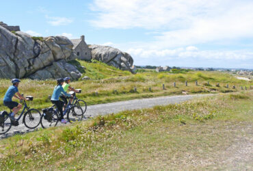 Un groupe de cycliste passe devant la maison entre les rochers de Menez Ham