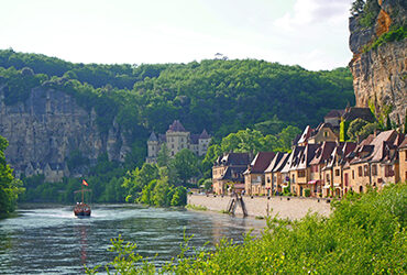 Vue sur les maisons troglodytes de la Roque-Gageac et sur la Dordogne traversée d'un bateau