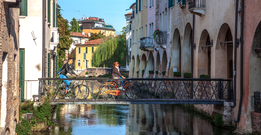 Un couple de cycliste traverse un pont au milieu de maisons colorees