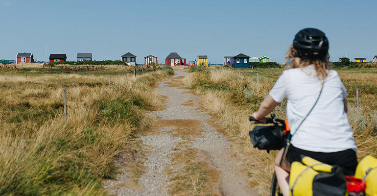 Un cycliste roule en direction de cabanes de plages colorées