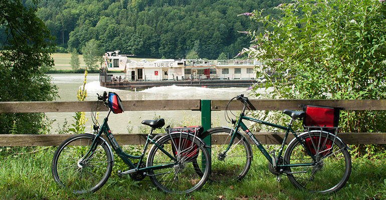 2 vélos tout équipé posé le long d'une barrière avec en arrière plan un bateau navigant sur le Danube