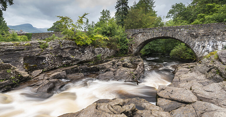 Rivière entourée de rochers et surmontée d'un pont en pierre