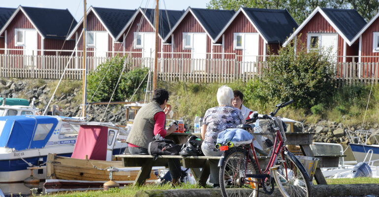 Un groupe de cycliste pique-nique sur une table dans un petit port et ses maisons rouges
