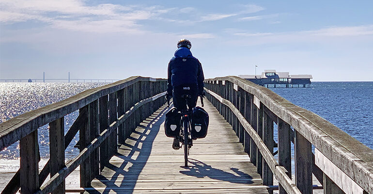 Un cycliste traverse un pont en bois au dessus de la mer