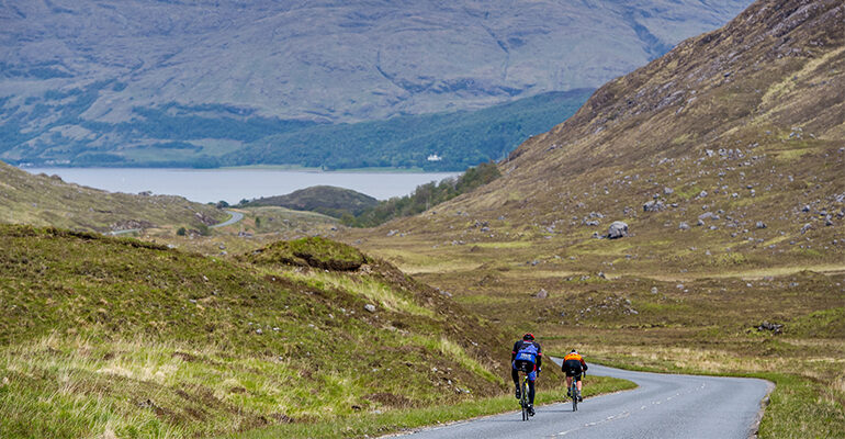 Deux cyclistes descendant une route de montagne vers un lac
