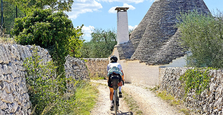 Une cycliste roule sur un chemin menant à une maison à trulli