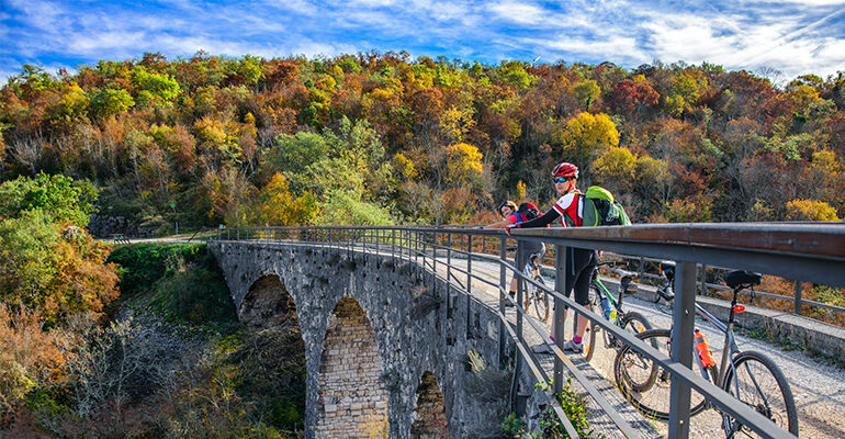 Cycliste à l'arrêt admirant un paysage forestier depuis un pont en pierre