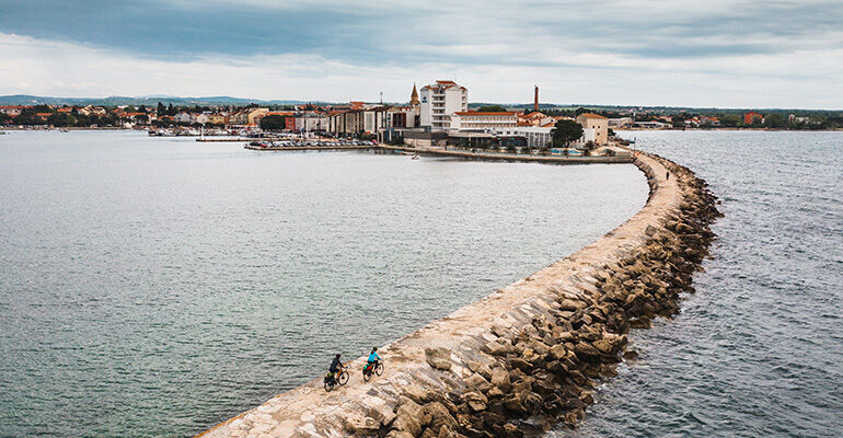 Deux cyclistes longent la digue entourée de la mer Adriatique