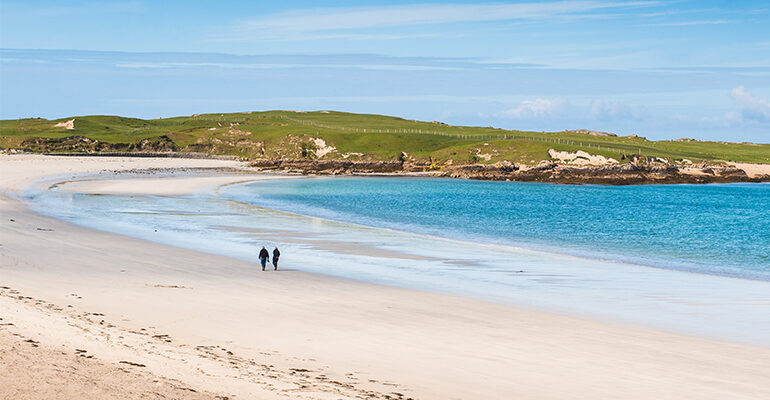 Deux personne marche sur une plage de sable blanc devant mer et montagne