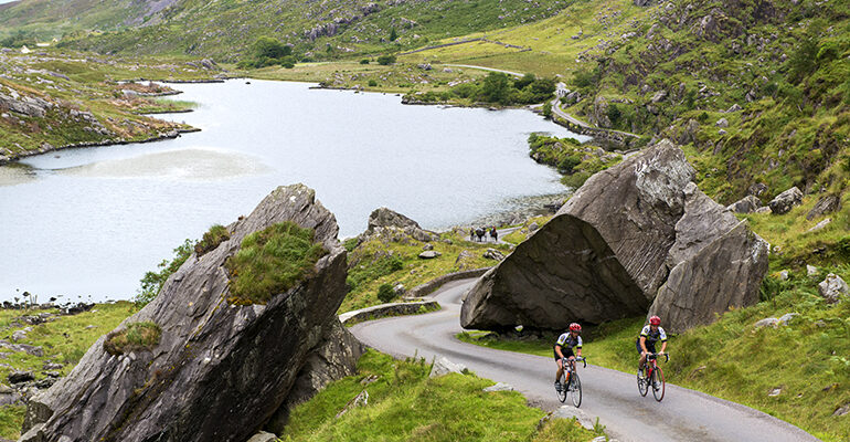 Groupe de cyclistes sur une route sinueuse entouré de lacs et montagnes