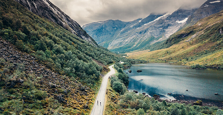 Deux cyclistes sont sur une route en Norvège, entourée de Montagnes et d'un lac