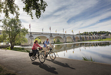 Un couple de cyclistes roule le long de la Loire et son majestueux pont de pierres