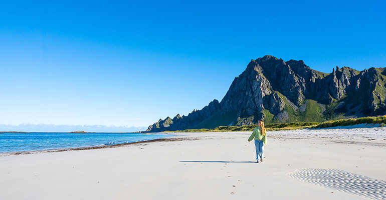 Une femme se promène sur une plage de sable blanc surplombée d'une falaise