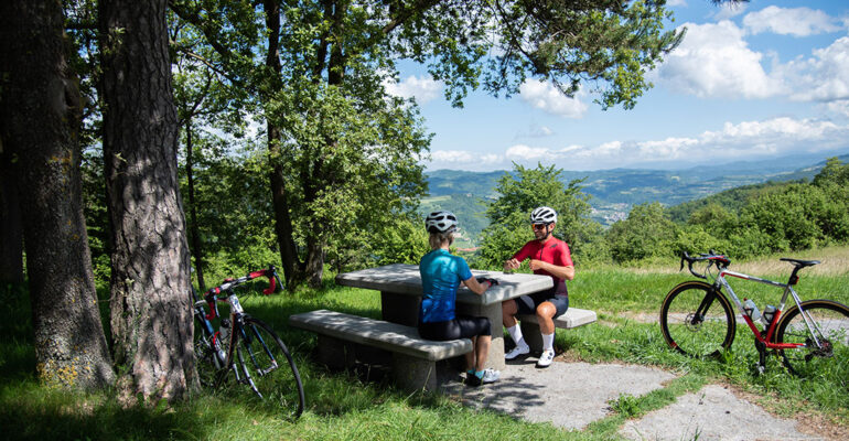 Un couple de cyclistes fait une pause sur un table de pique-nique entouree de vignes