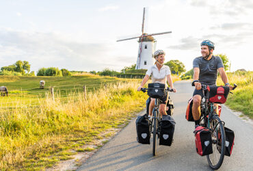 Deux cyclistes sur le chemin de halage avec un grand moulin derrière eux