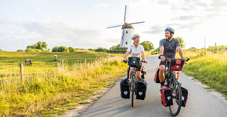Deux cyclistes sur le chemin de halage avec un grand moulin derrière eux