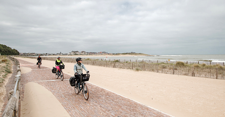 Un groupe de cyclistes longe une plage de sable blanc