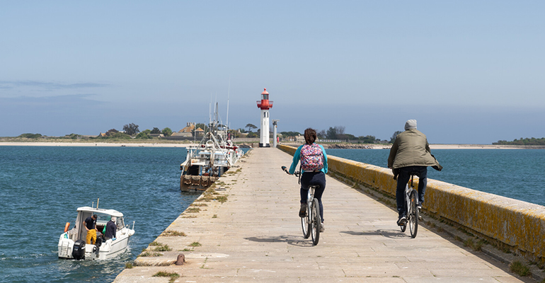 Un couple de cycliste se dirige vers un phare et son port