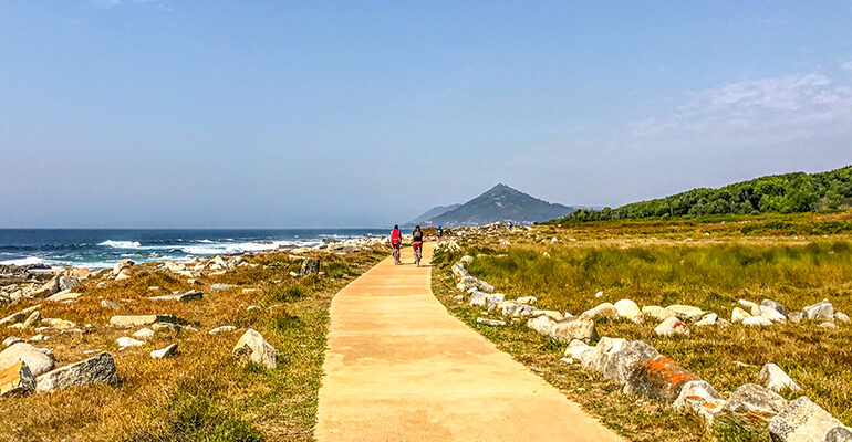 Deux cyclistes sur une piste bordée par la campagne et la mer