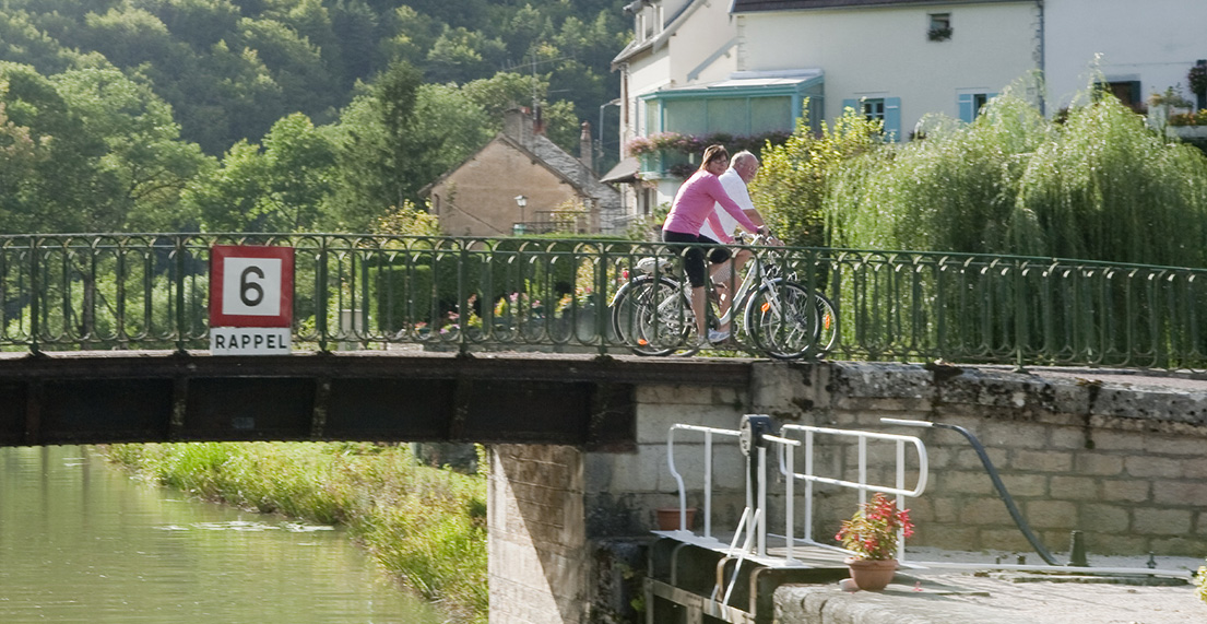 Un couple de cycliste traverse un canal fleuri sur un pont