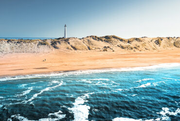 Vus panoramique sur une plage bordée par la mer turquise et son phare