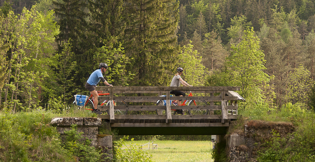 Un couple de cycliste traverse un pont en bois au milieu d'une foret