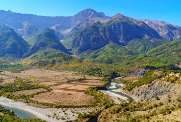 Vue aerienne d'une riviere aux eaux turquoise qui s'ecoute entre plaines et montagnes