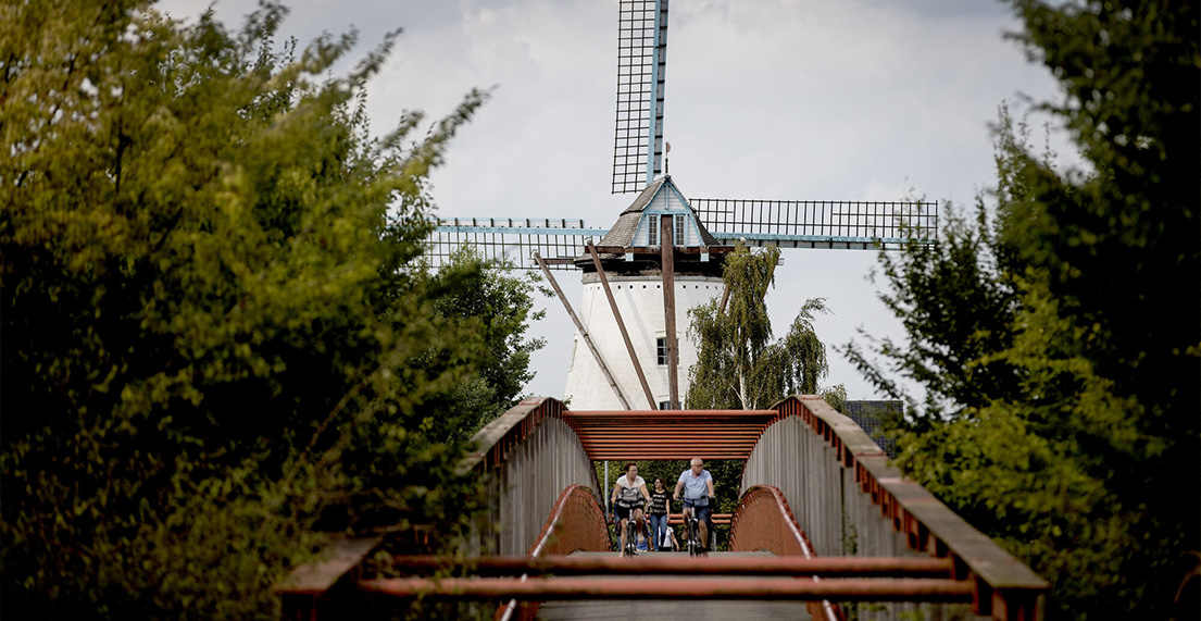 Un groupe de cyclistes traverse un pont avec un moulin a vent derrièee eux