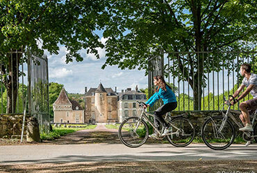 Un couple de cycliste roule sur un chemin bucolique et devant un chateau
