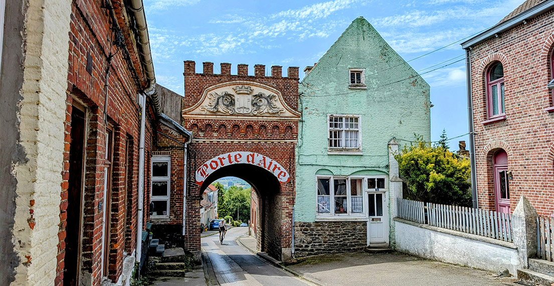 Un cycliste traverse les rues pavees de Cassel et ses batiments en briques rouges