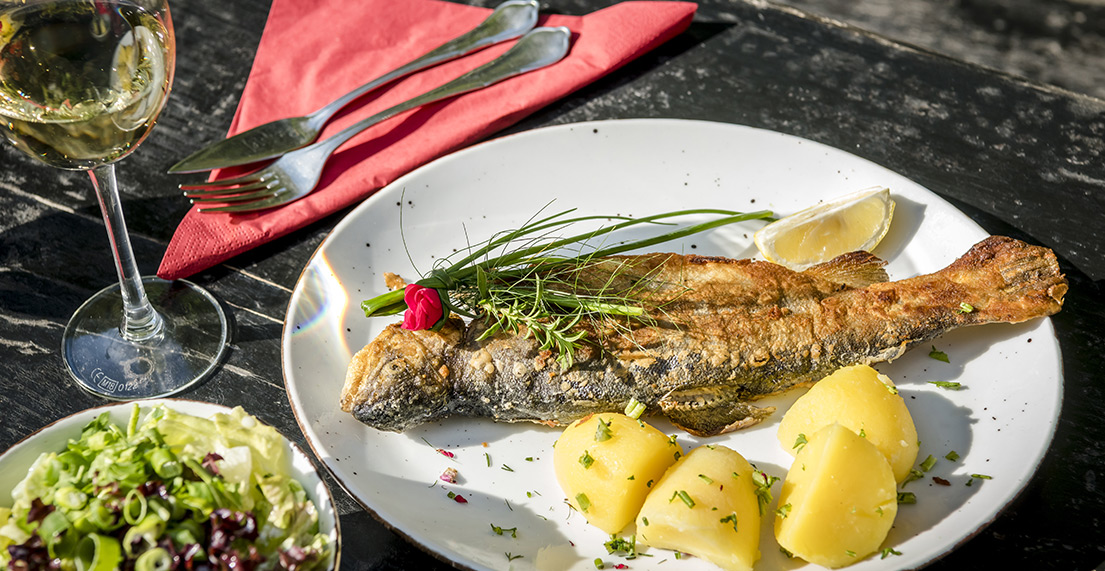 Une assiette de poisson grillé servie avec des pomme de terre et un verre de vin blanc