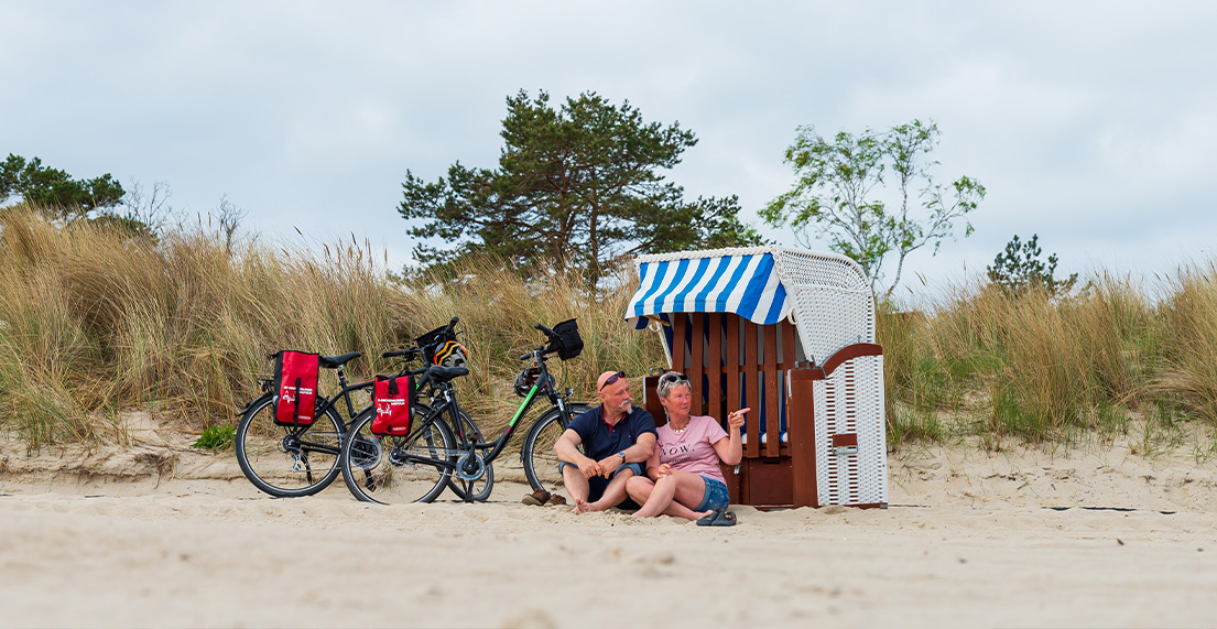 Un couple de cycliste se repose sur une plage de sable blanc