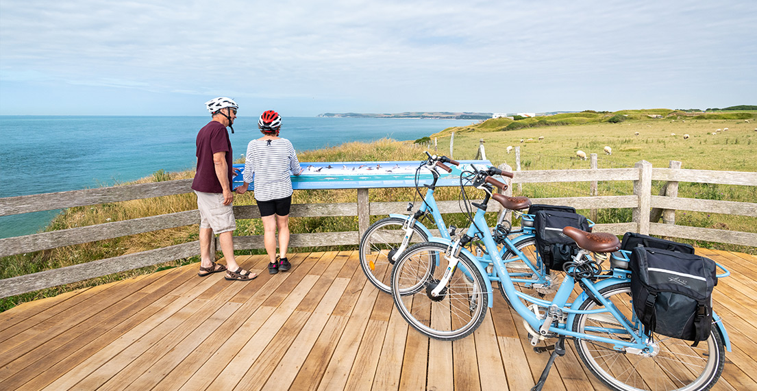 Un couple de cycliste admirent la cote, ses falaise et la mer depuis une plateforme en bois