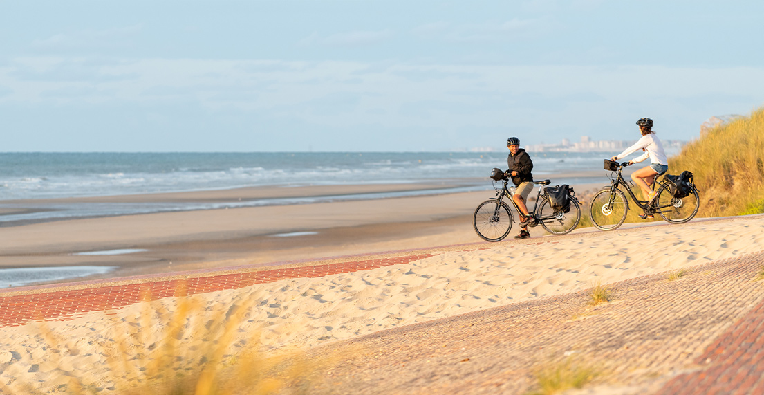 Un couple de cycliste avance sur une plage de sable fin avec leurs velos